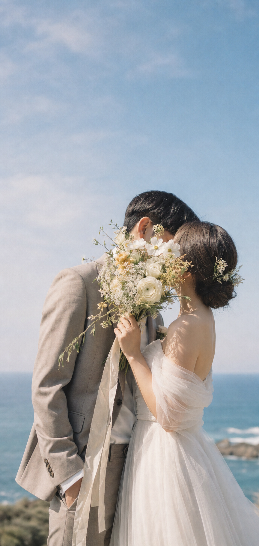 Pareja de novios junto al mar, cubierta por un ramo de flores blancas
